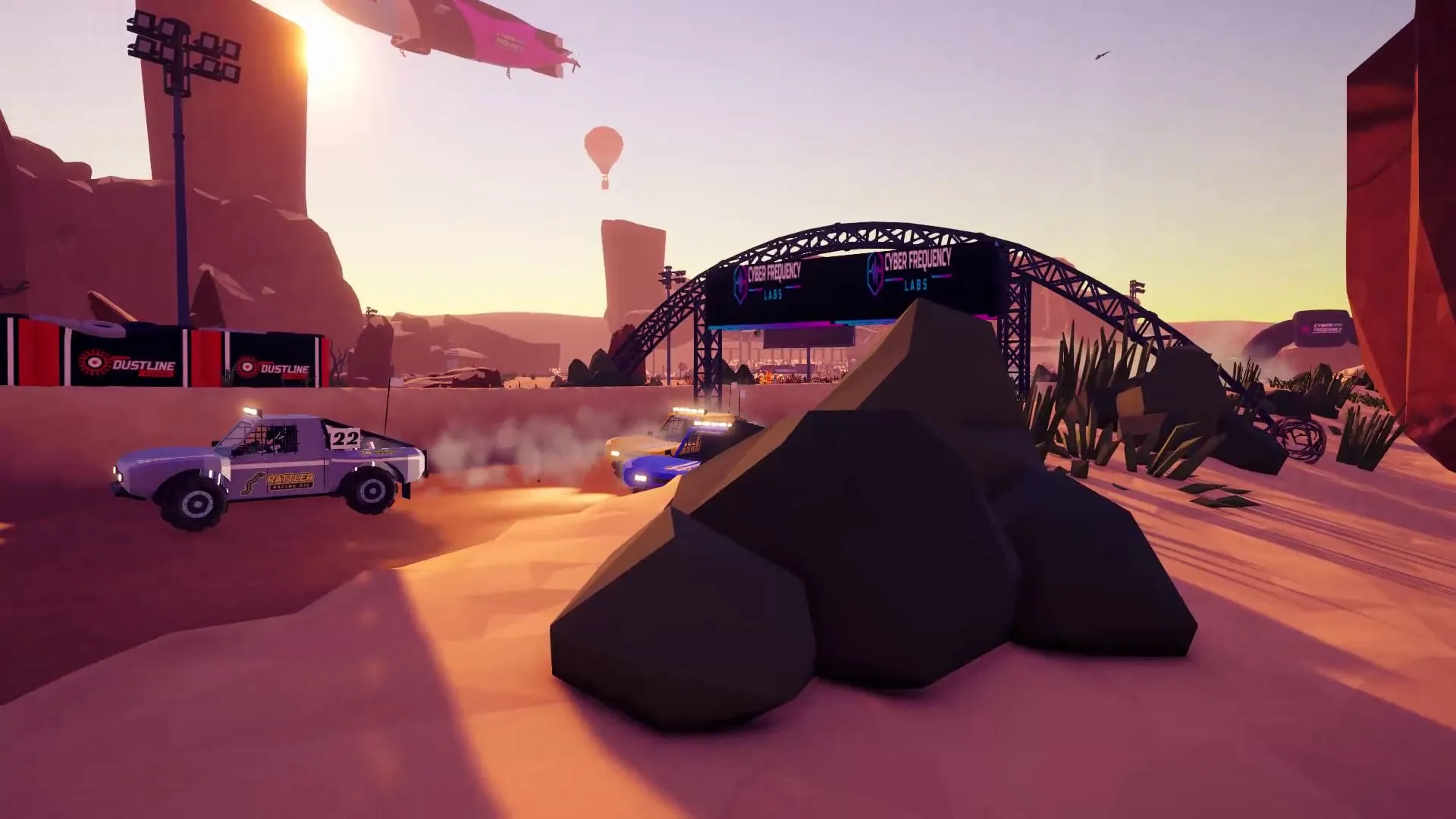 Trophy trucks racing past a race-day arch on a sunset desert track